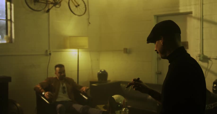 Two men sit inside a house and smoke and talk