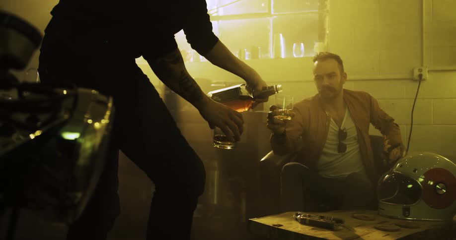A man pours a drink for another man indoors