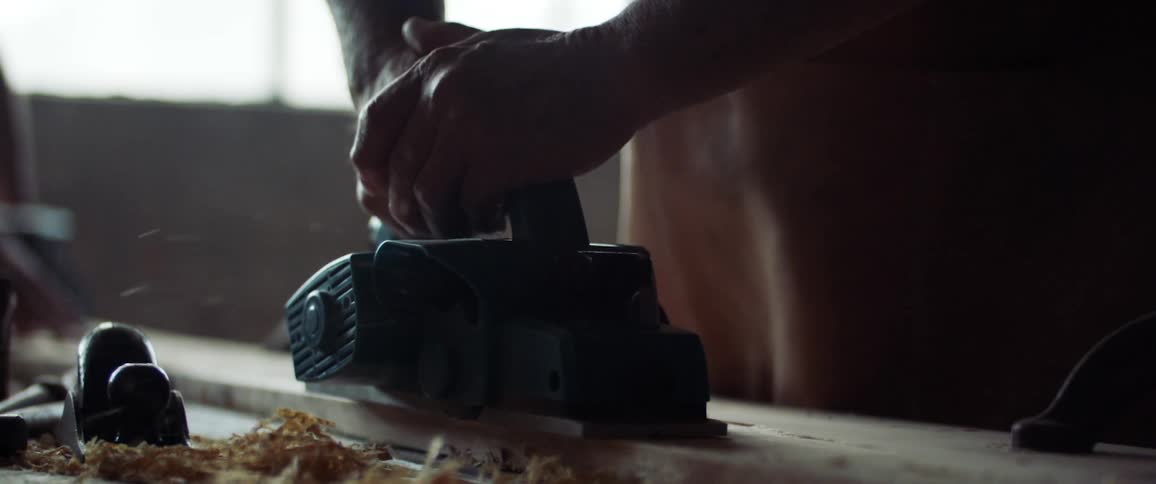 Man sands a plank of wood using a power tool in a workshop