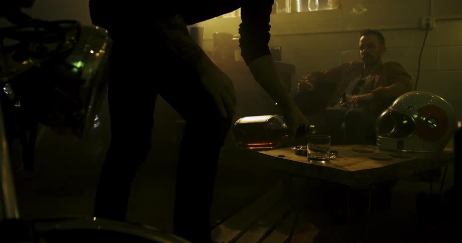 A man sits and smokes in a home while another person pours a drink