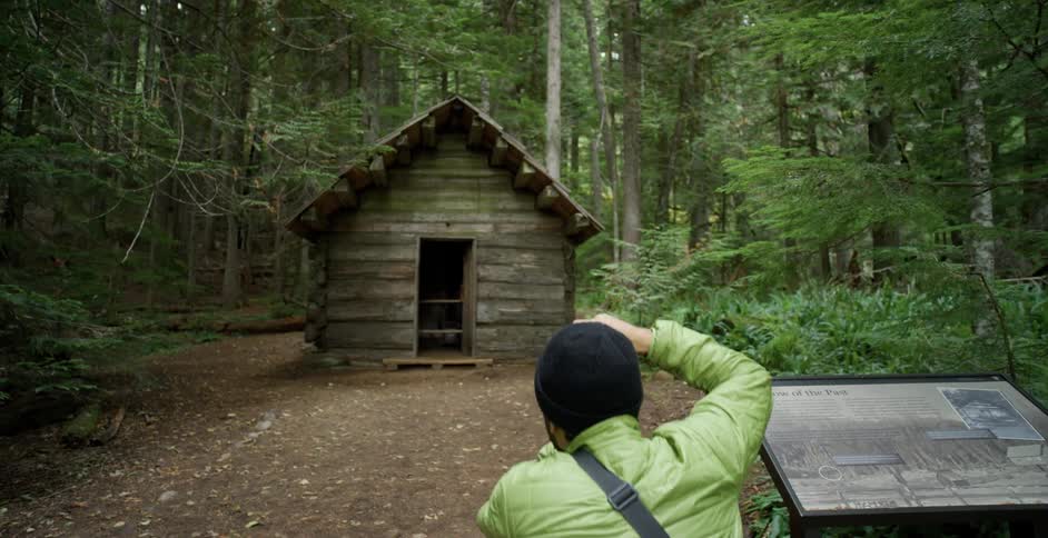 A man takes pictures of a small shack in a forest