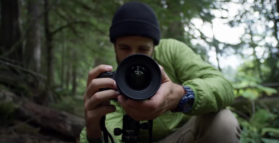 A man is aiming his camera in the forest