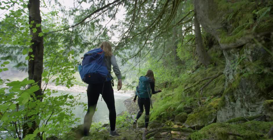 Two white women hike along the shore of a river