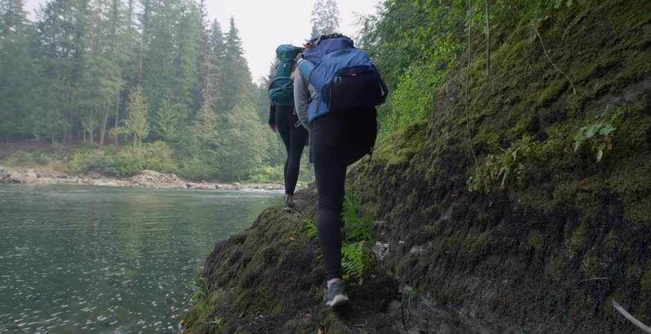 Hikers hiking on edge of rocks near shoreline of a lake