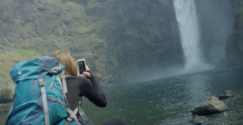Young woman takes pictures of a waterfall with her phone