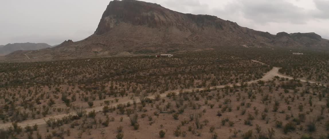 A building in the sparse badlands below a mountain on a cloudy day
