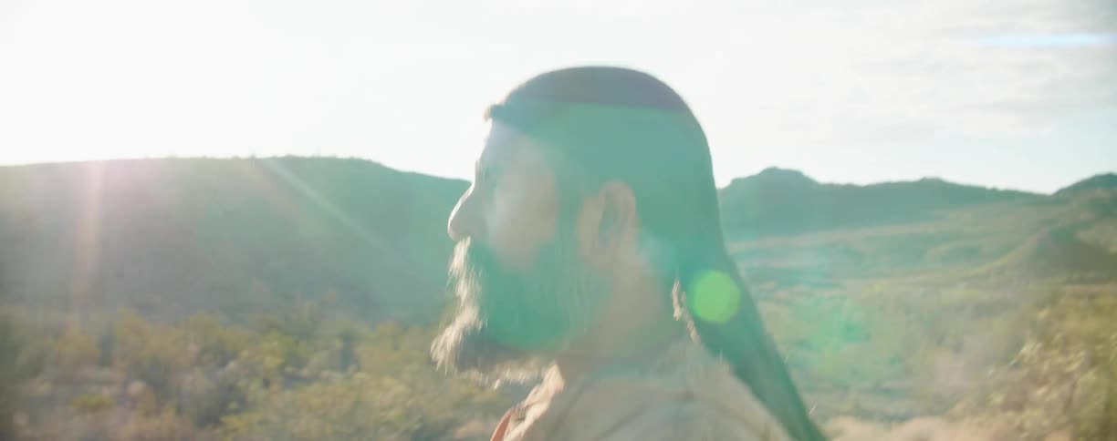 A man walking in the desert with mountains the sky and clouds in the background