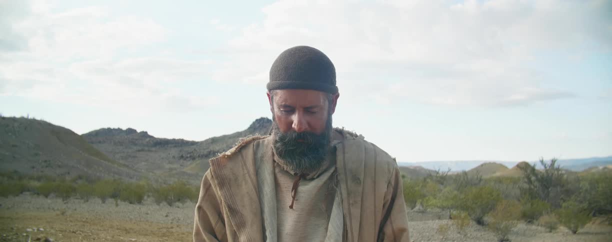 A man standing in the desert with trees mountains sky and clouds in the background