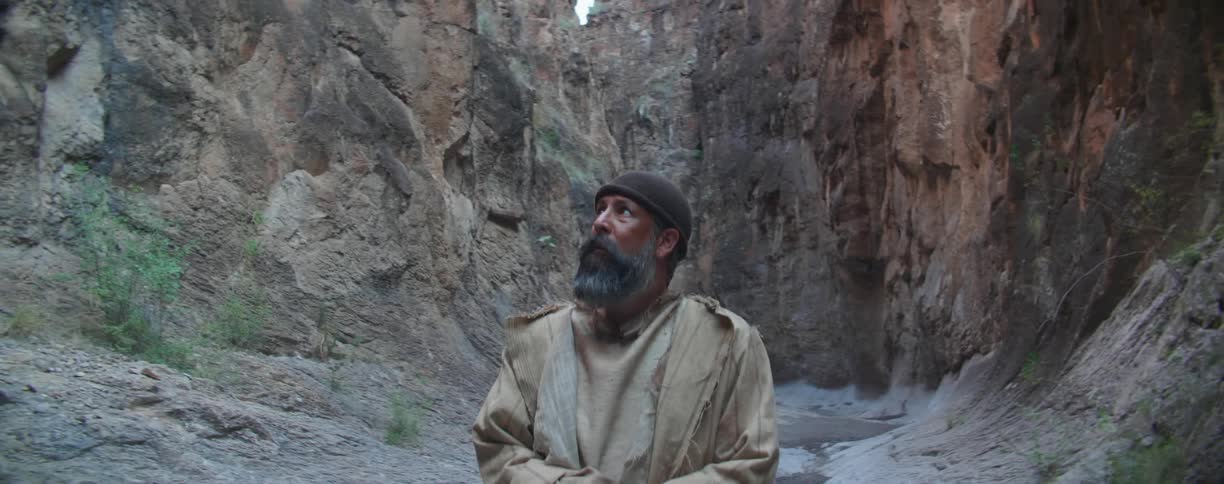 A man cautiously walks through the base of a canyon and looks up and down