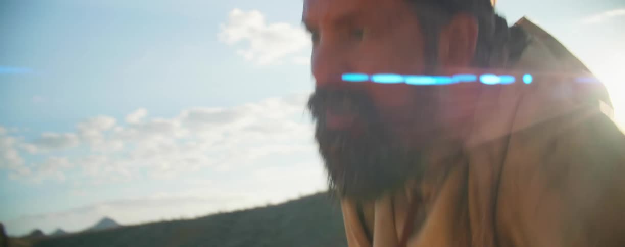 A white man in ratty clothing scrambles up a slope in a desert
