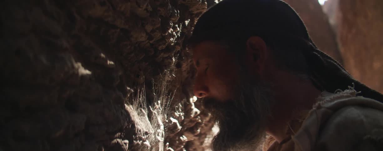 A man in a canyon resting his head on a cliff with cobwebs