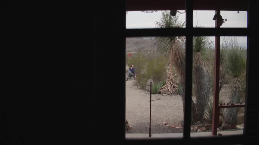 A window with a person sitting outside with the sky and mountains in the background