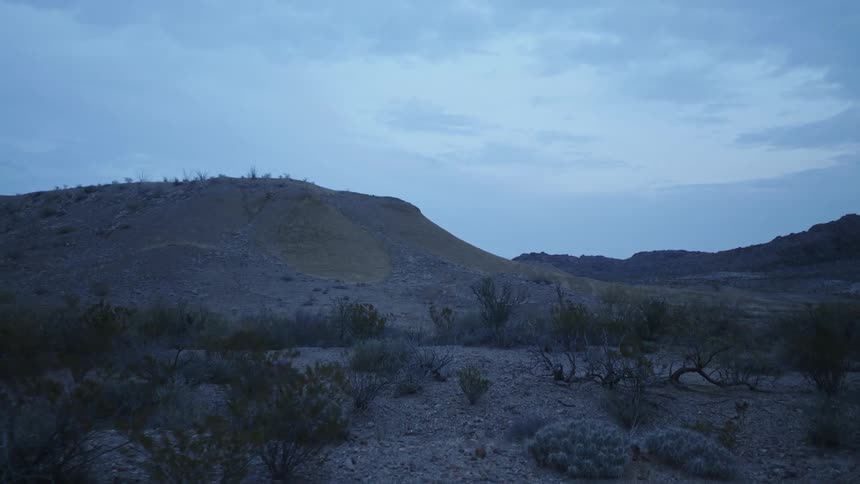 Scrub dots a desert area near a hill and mountains