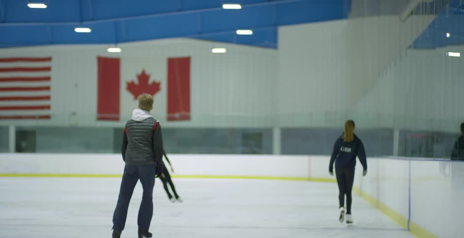 Three white people ice skate at an indoor ice rink
