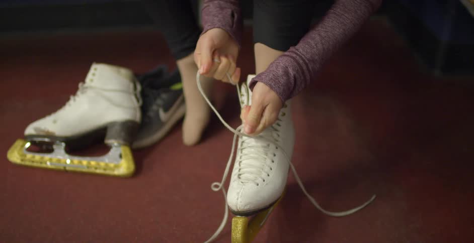 Female with one ice skate on tightens the laces as she places them in the eye hooks of the boot