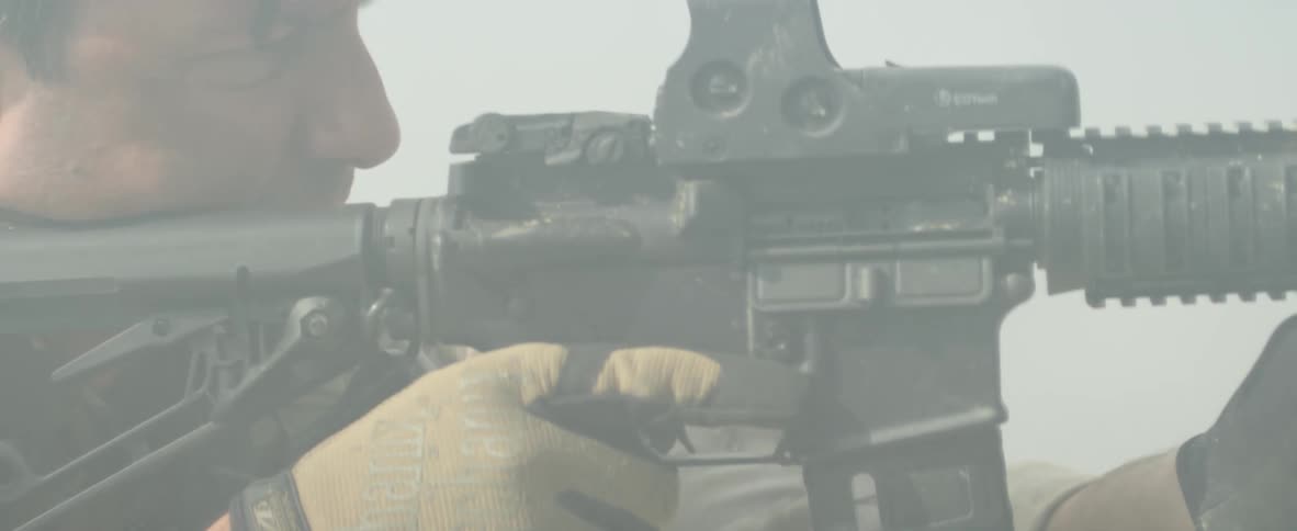 Man shooting an assault rifle surrounded by dust or smoke