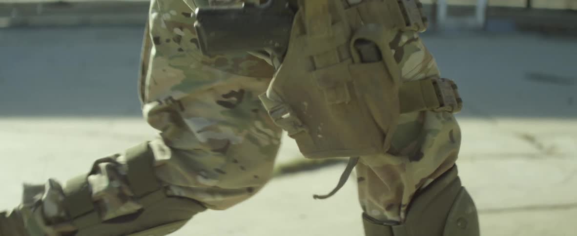 A person with army fatigues boots and a pistol running