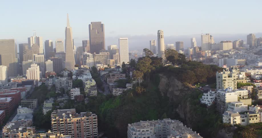 Buildings nestle around low mountain near city center with haze on the horizon