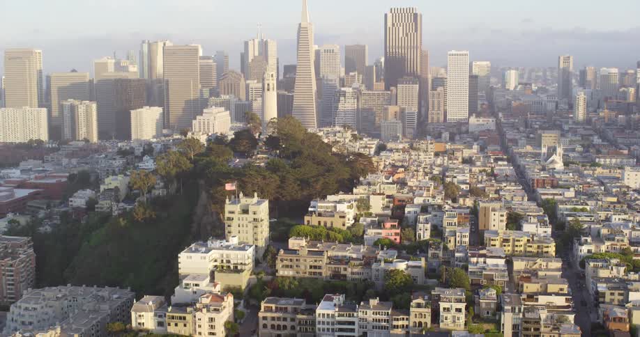 Skyscrapers and towers stand behind rooftops of city neighborhood buildings