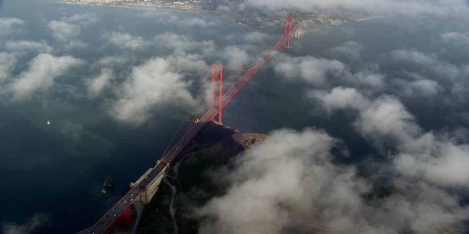 Aerial view of vehicles crossing the golden gate bridge under white clouds