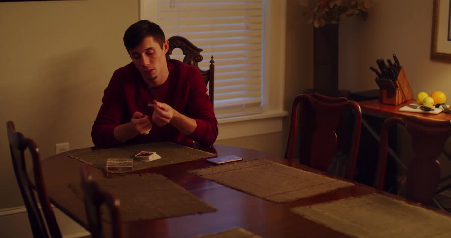 A man sitting at a dining room table smoking a cigarette