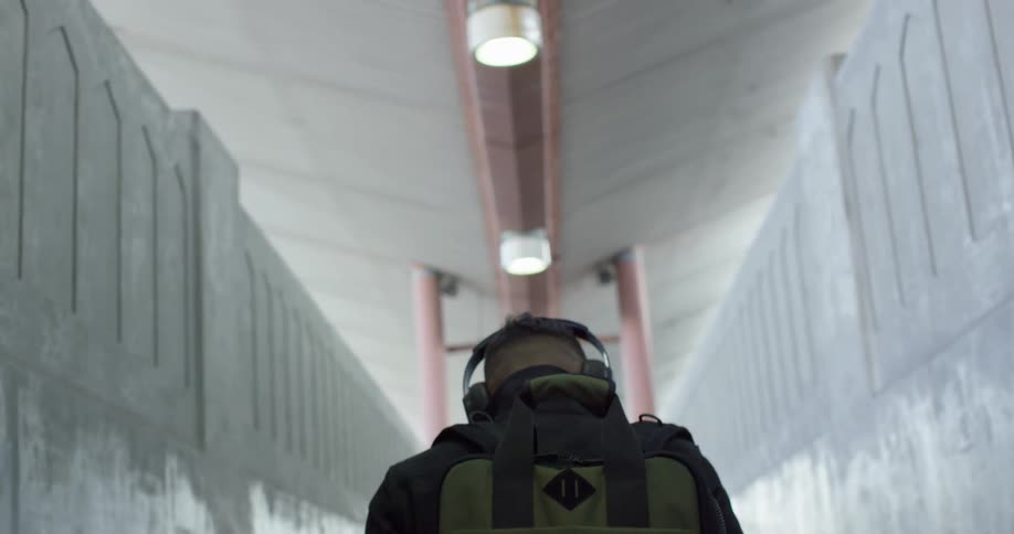 A man wearing headphones and backpack ascends a staircase between two stone walls
