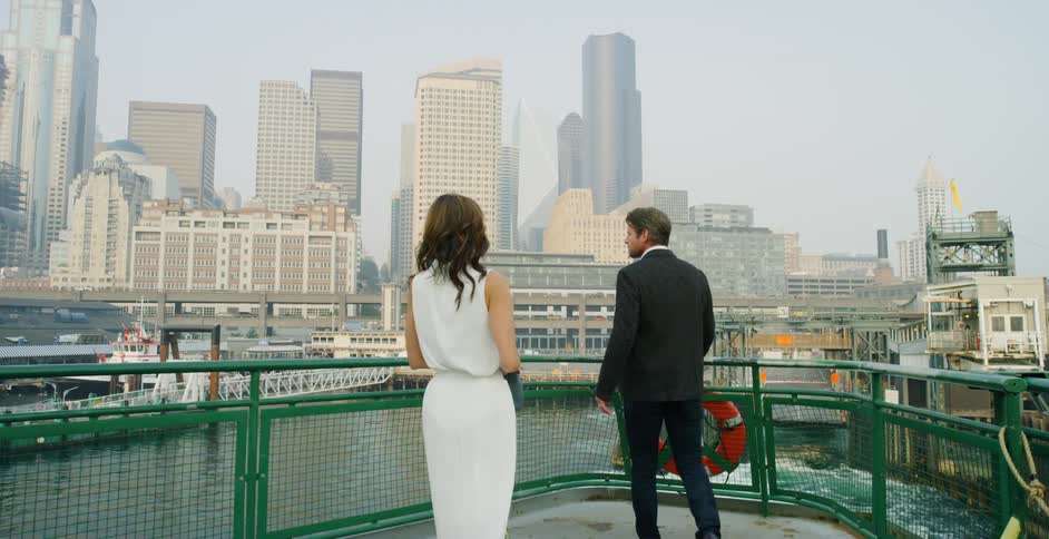 A woman runs towards her husband and puts her arm around him as they watch the boat they are on pull away from the dock