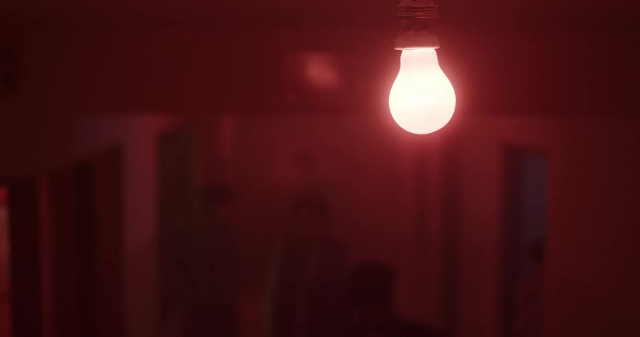 A lone light bulb burns in a fixture in an indoor area where males wander around