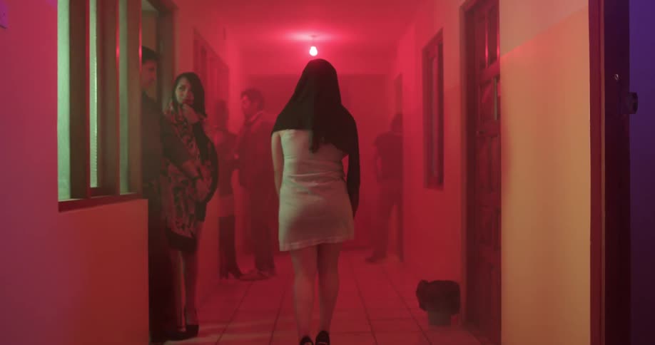 A woman walks down a busy hallway illuminated by a red light in a club