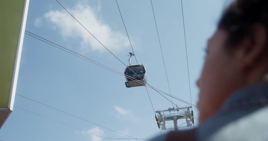 Woman wearing jean jacket looks around as cable car passes overhead