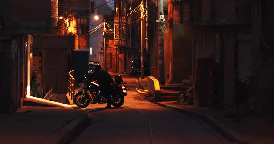 Person wearing helmet pushes motorcycle off street through door at night