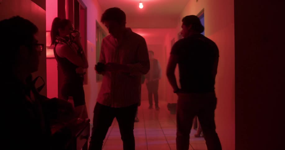 Men in a brothel hallway with red lights talk to women