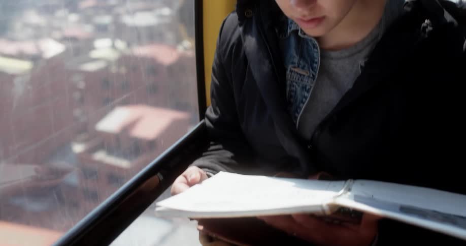Woman reads notes in notebook while riding a cable car over the city