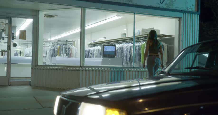 A woman walking out of a car and walking towards a store window and looking at a television set