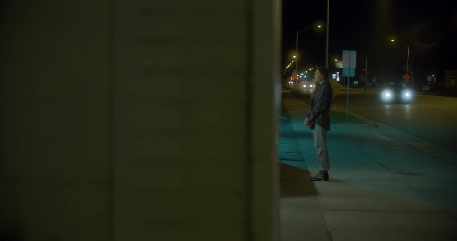 Woman with brown hair and a black shirt stands on a pavement in front of a store at night