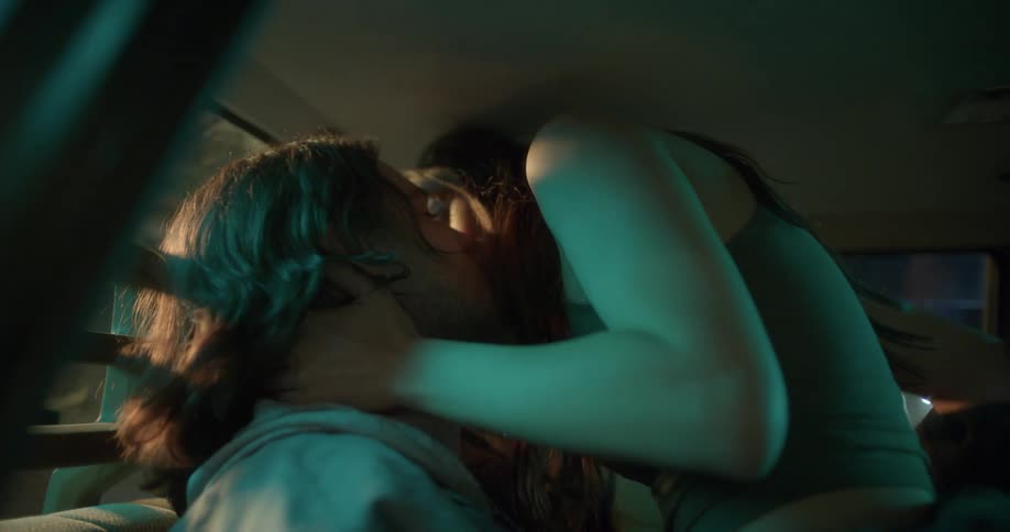 A man and a woman make out in the back seat of a car