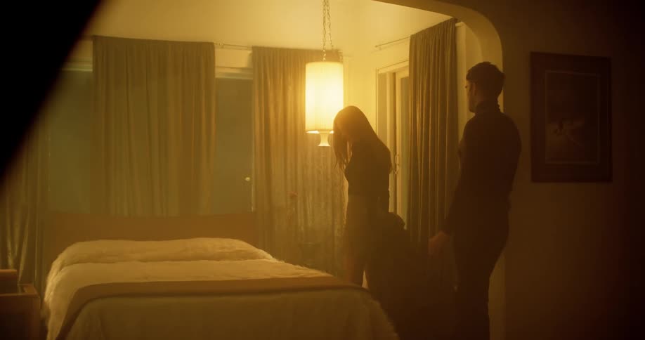 Man and woman stand near bed as she removes and drops coat