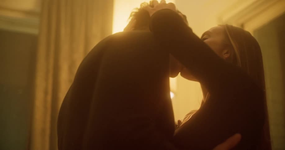 Man and woman gently kiss in a room near the yellow golden light of a lamp