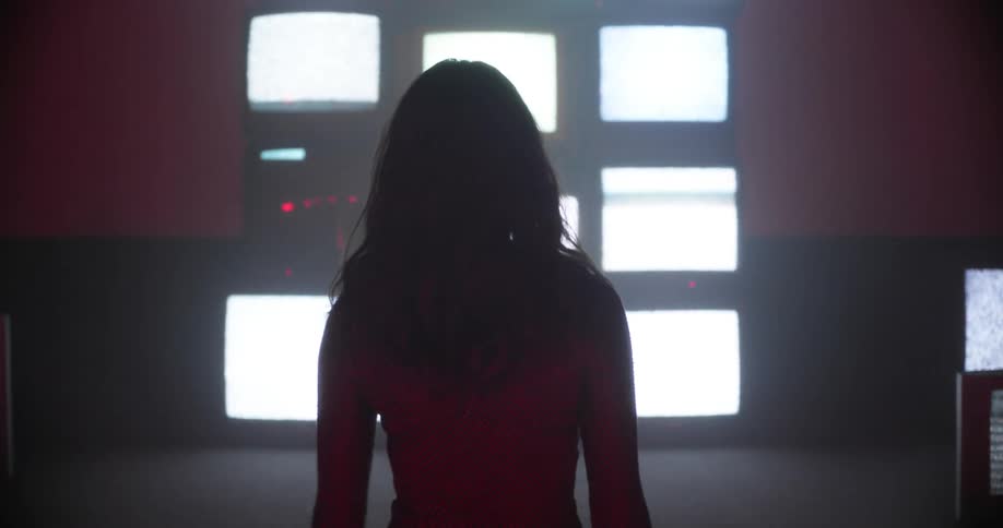 A woman walks toward a wall filled with televisions