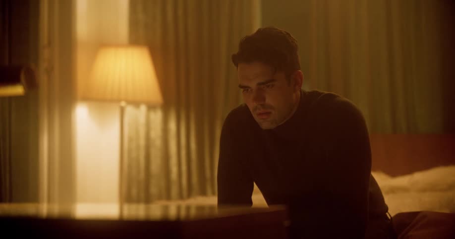 Man with a black turtleneck sweater sits on a bed and feels depressed in the bedroom
