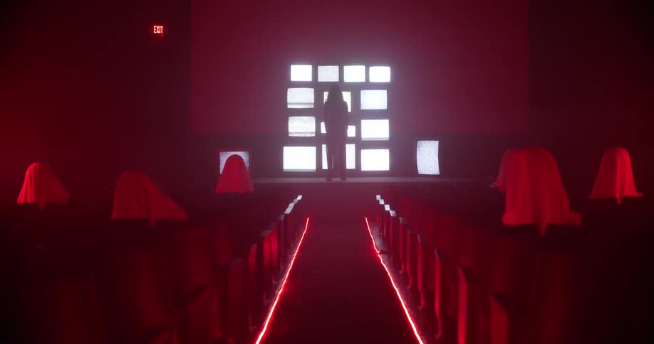 A person stands at the front of a dimly lit room