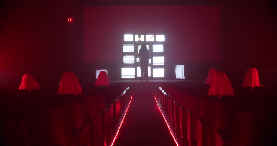 Woman stands in front of a tower of television screens showing static in the stage of a theatre