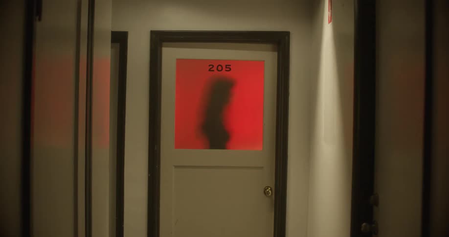 Silhouette of a woman on a red backlight through the window on a door in a corridor