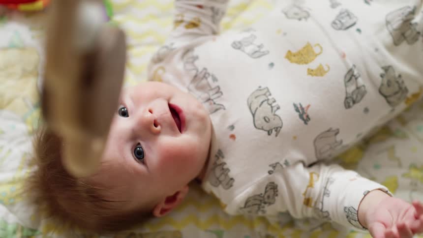 Baby lies in cradle and looks at spinning colorful toy carousel