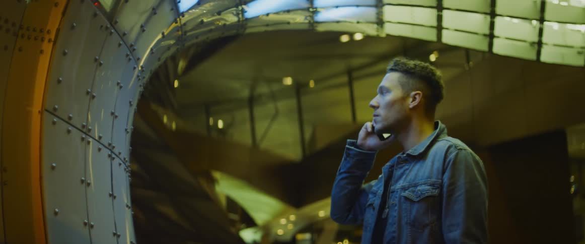 Man answers a phone call in his smartphone near a futuristic building at night