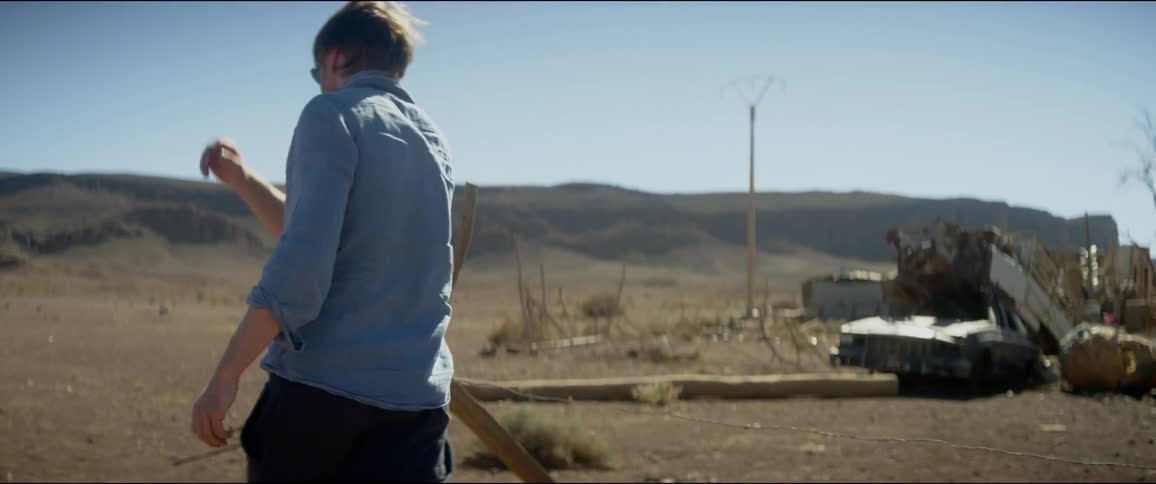 A man walks through a deserted rural area and throws a stick
