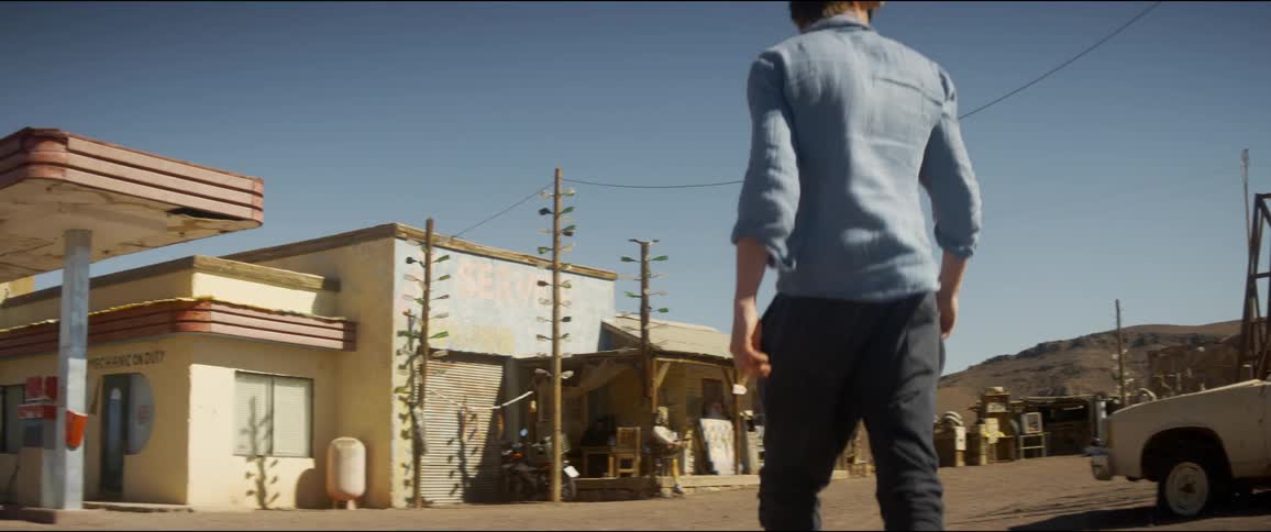 A man walking in the desert towards a gas station with the sky in the background
