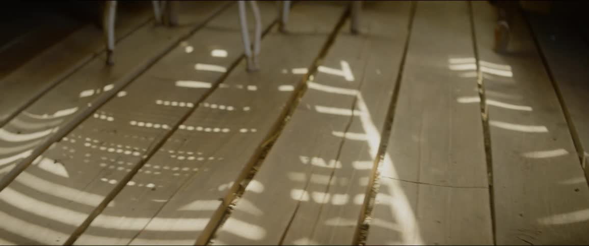 Light filters trough window casting shadow on wooden floor boards near chair legs