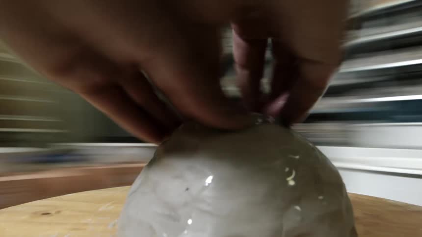 Hands work on a mound of clay as something spins nearby