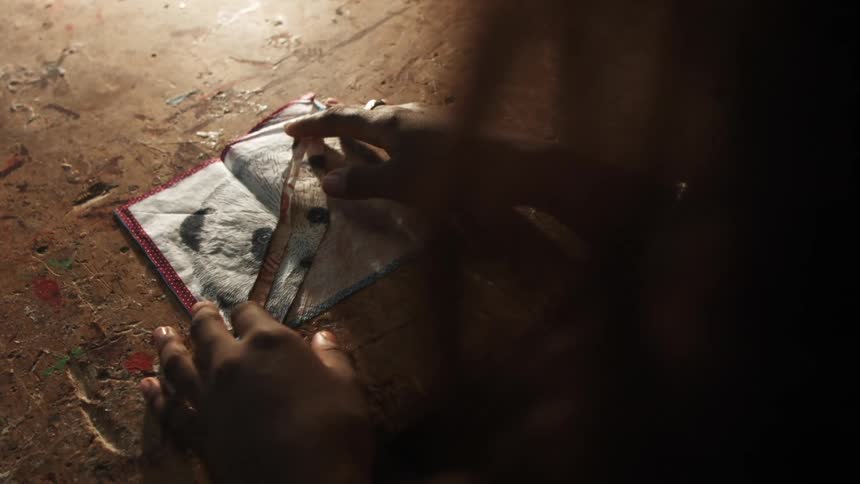 A girl places a drawing on a table and folds a corner back to reveal another sketch